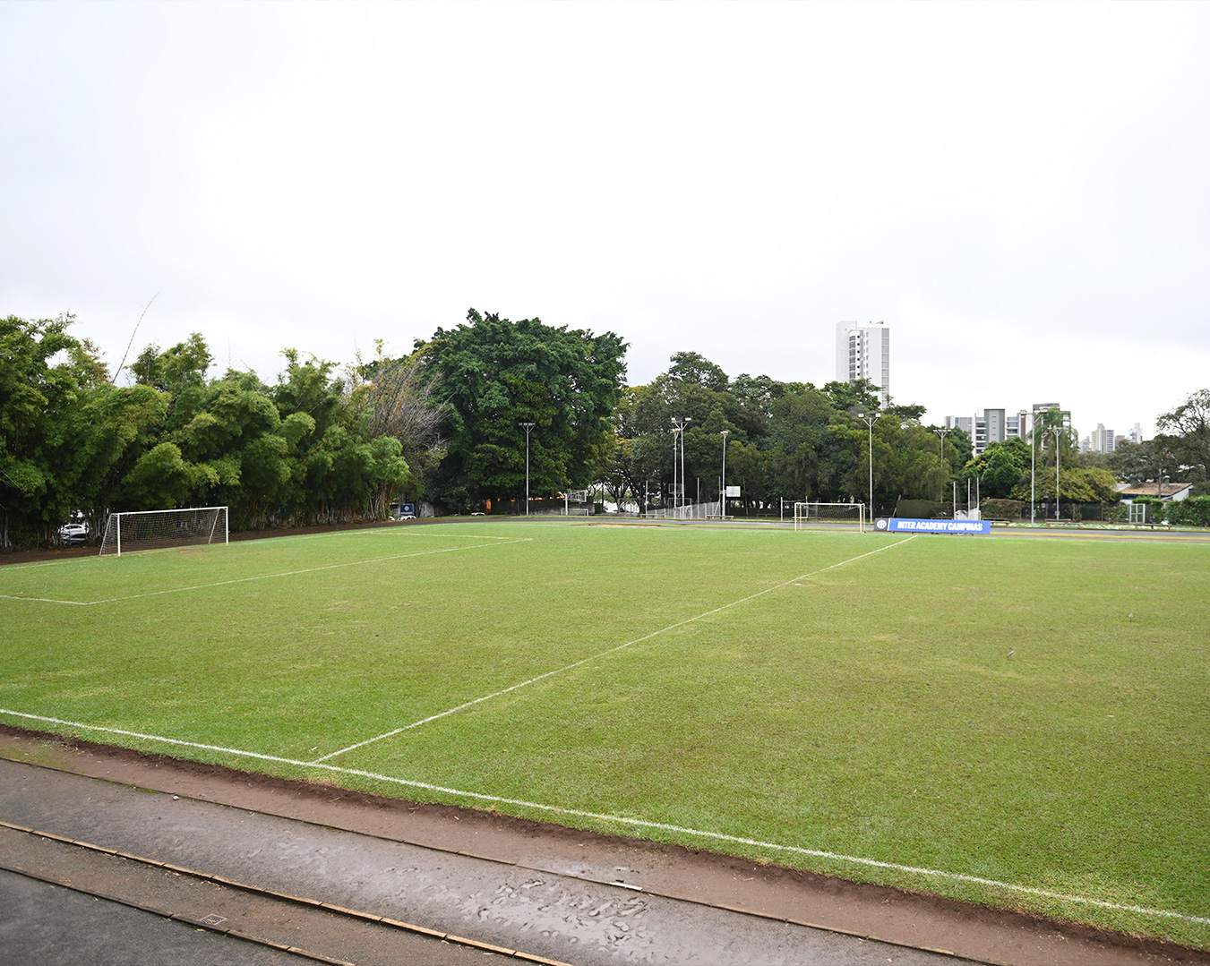 Campo de futebol gramado do colégio com traves nas duas extremidades, arborizado nas laterais