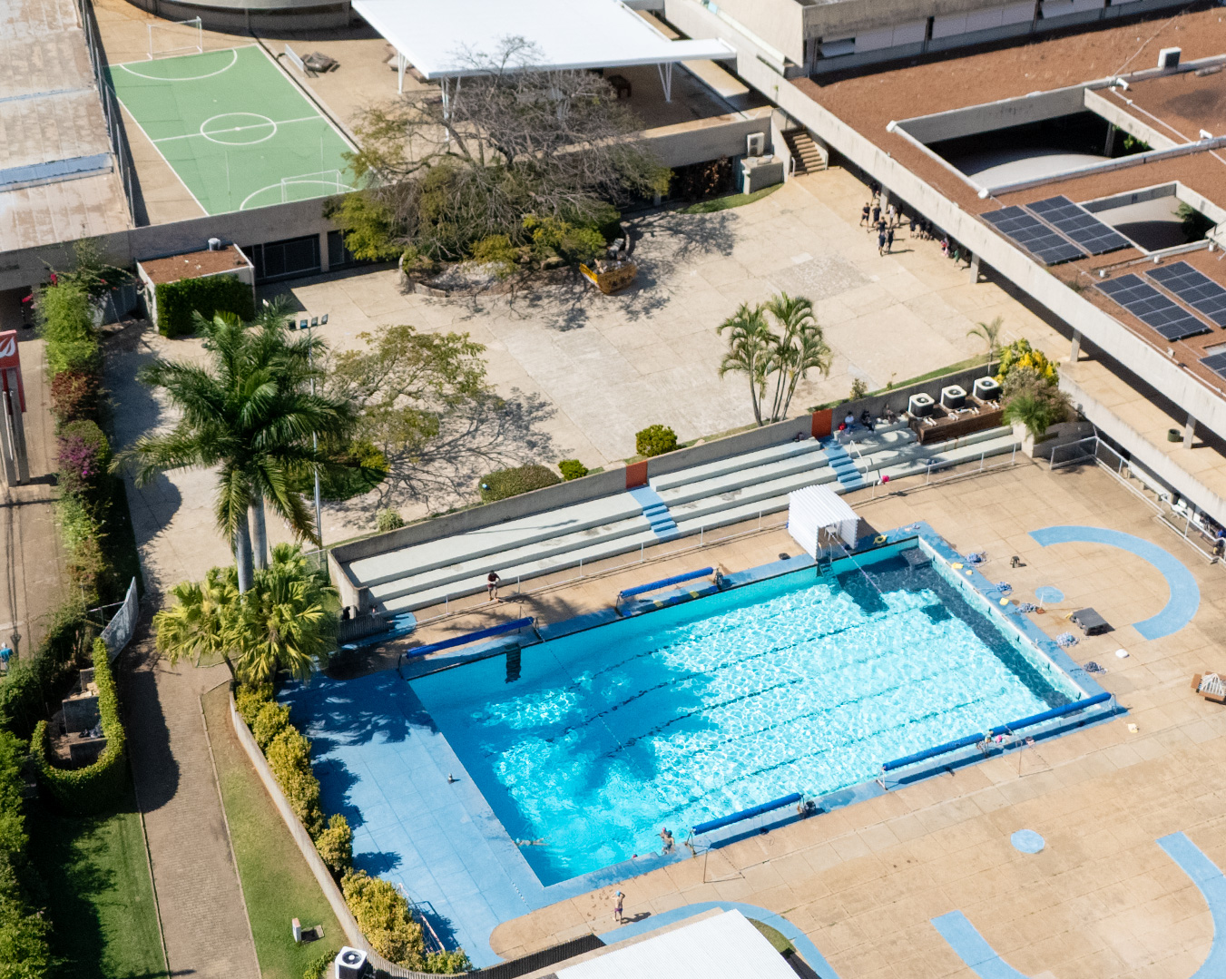 Vista aérea da piscina semiolímpica do colégio com raias demarcadas, ao lado da quadra e das áreas verdes do campus