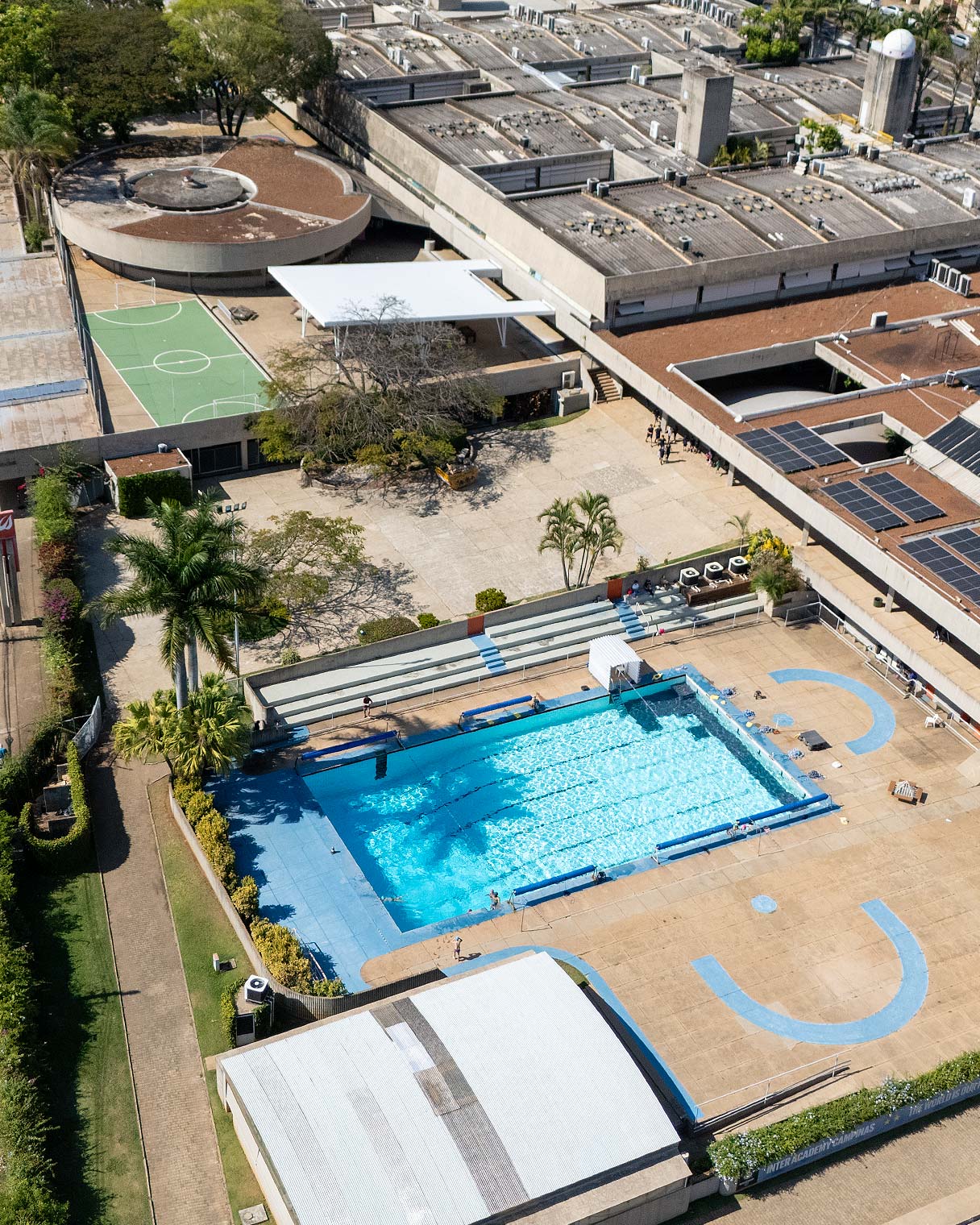 Vista aérea do campus mostrando a piscina semiolímpica com raias, a quadra ao lado e os prédios do colégio ao redor